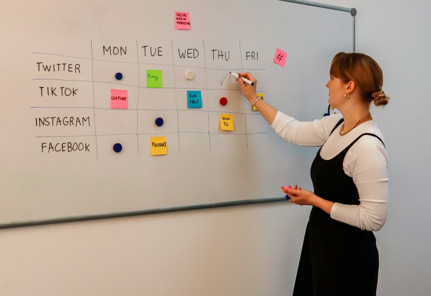 Woman checks off social media plan on a content calendar whiteboard.